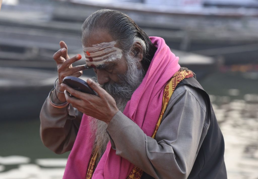 A man checks in a pocket mirror as he applies Hindu religious markings to his forehead on the ghats beside the sacred Ganges River in Varanasi. (Richard McGuire photo)
