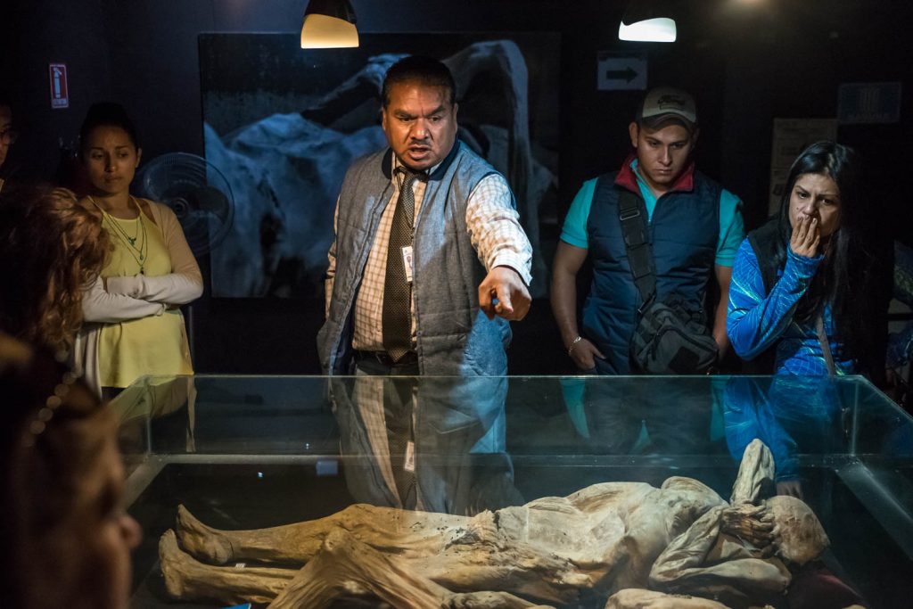 A tour guide points to some of the finer details in a group of mummies, some of whom died violent deaths. Museo de las Momias, Guanajuato, Mexico. (Richard McGuire Photo)